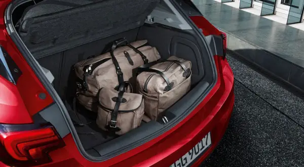 Bagażnik czerwonego Opla Astry J hatchback wypełniony trzema stylowymi torbami podróżnymi.