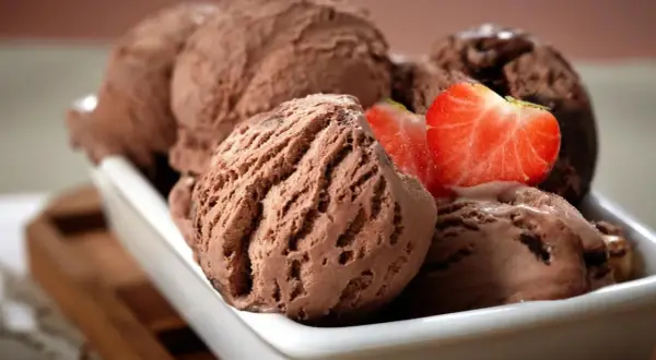 Cremoso helado de chocolate servido en un cuenco blanco, decorado con fresas frescas.
