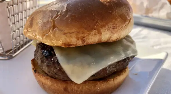 Hamburger z serem na białym talerzu, obok koszyka na frytki.