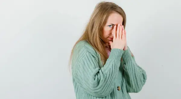 Een vrouw met blond haar, die haar gezicht bedekt met haar handen, lijkt overprikkeld, wat kan duiden op hsp en trauma.