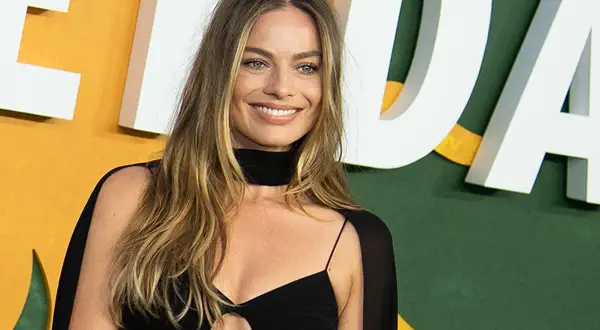 Margot Robbie sonríe con un vestido negro. La pregunta de cuanto mide Margot Robbie es un misterio, pero su estilo es innegable.