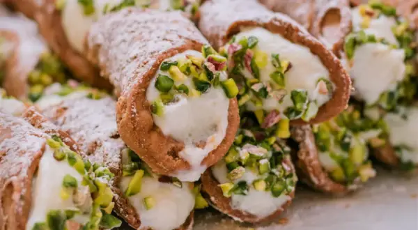 Stos delikatnych, włoskich rurek z kremem i pistacjami, posypanych cukrem pudrem.