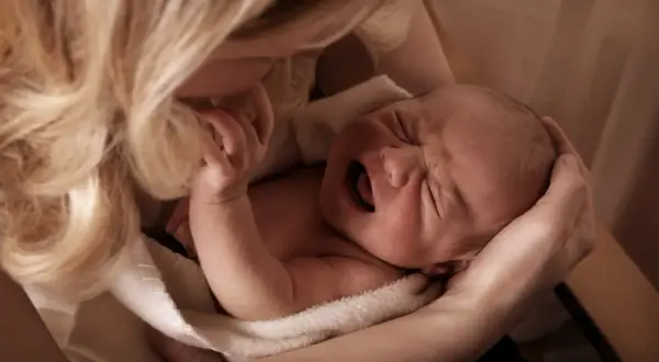 Matka tuli płaczące dziecko, szukając sposobu, jak odczynić urok na dziecku. Delikatne dłonie i włosy otulają maluszka.
