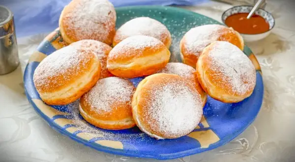 Ein Teller voller frisch gebackener Krapfen, bestäubt mit Puderzucker. Dieses Krapfen Rezept ist ein Genuss!