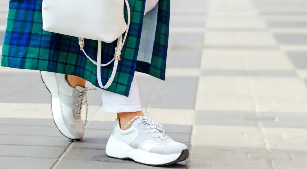 Stylowe białe sneakersy damskie idealnie komponują się z białą stylizacją i zielono-niebieską kraciastą marynarką.