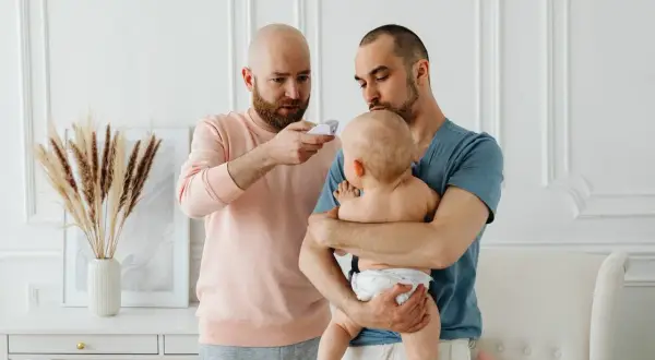 Två pappor kollar febern på sitt koksalt bebis med en termometer.