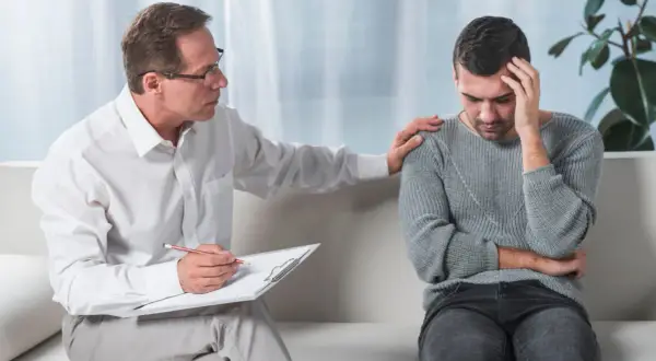 Psycholog dla dorosłych wspiera mężczyznę w trudnych chwilach. Terapeuta kładzie dłoń na ramieniu pacjenta, okazując zrozumienie i troskę.