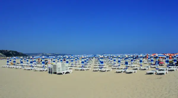 Plaża w Albena Bułgaria, rzędy leżaków i parasoli w niebiesko-białe pasy pod błękitnym niebem.
