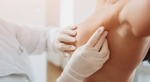 Lekarz w białej rękawiczce delikatnie bada pierś, lokalizując znacznik tytanowy po biopsji.