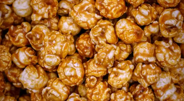 Gros plan sur une montagne de pop-corn caramel, chaque grain enrobé d'une sauce dorée et brillante. Un délice croustillant et sucré.