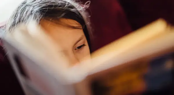 Niña concentrada en la lectoescritura, página de libro abierto.