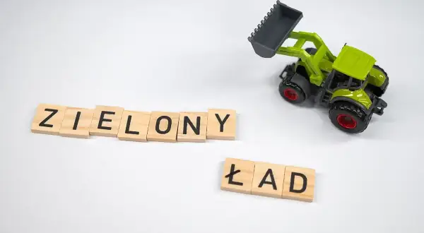 Drewniane klocki z literami "ZIELONY ŁAD" i zielona zabawka koparka na białym tle.