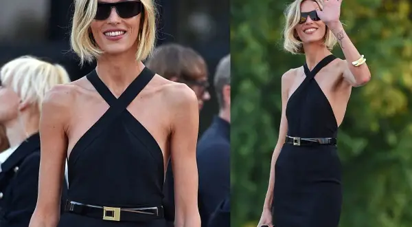 Elegancka kobieta w czarnej sukience i okularach przeciwsłonecznych, z subtelnymi złotymi akcentami, jak bransoleta i klamra paska.