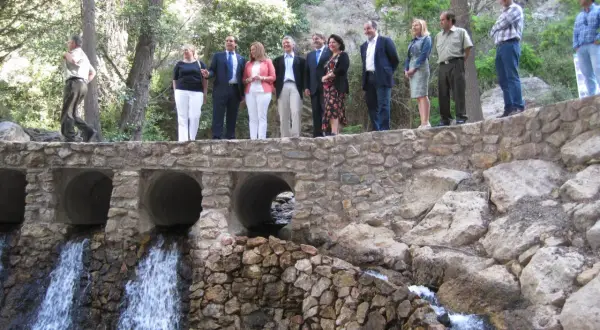 Un grupo de personas celebra en el lugar donde nace el río Andarax, con cascadas cayendo bajo un puente de piedra.