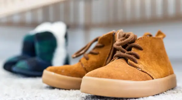 Brązowe, sznurowane buty dziecięce na pierwszym planie, w tle niebiesko-zielone botki w kratę.