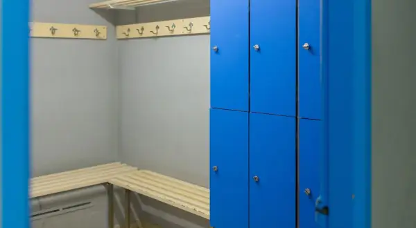 Un vestiaire avec des casiers bleus, des bancs en bois et des patères.
