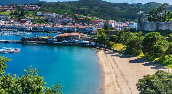 Bahía con barcos y un pueblo costero al fondo. Ideal para planificar como viajar barato por España y disfrutar de sus costas.