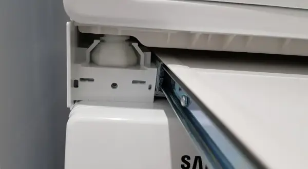 Zbliżenie na mechanizm łącznika suszarki na pralce Samsung, widoczny metalowy wspornik i biała podstawa.