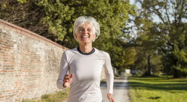 Femme souriante de 60 ans courant sur un chemin, suivant un plan d'entraînement course à pied.