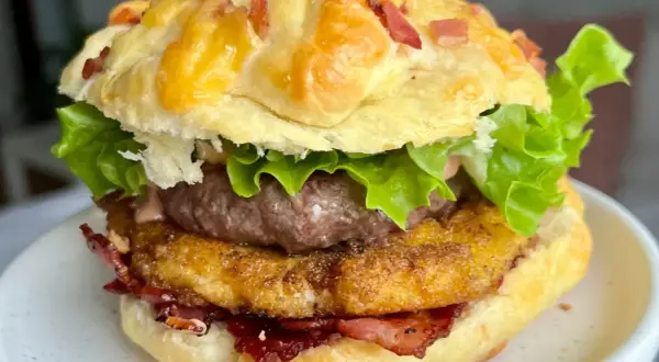 Domowy burger z serem, bekonem, kotletem i sałatą na talerzu.
