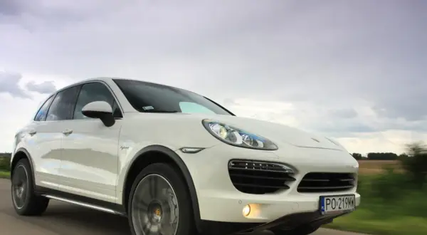 Biały Porsche Cayenne Turbo pędzi po drodze, chmury na niebie sugerują zmienną pogodę.