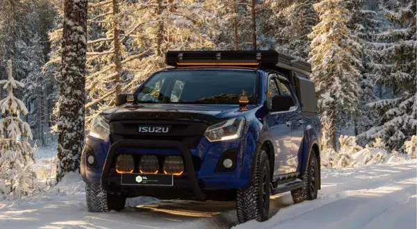 Niebieski Isuzu w zimowym lesie, z dodatkowymi światłami LED na dachu i zderzaku. Dowiedz się, jak ustawić żarówki LED w samochodzie, by podróżować bezpiecznie.