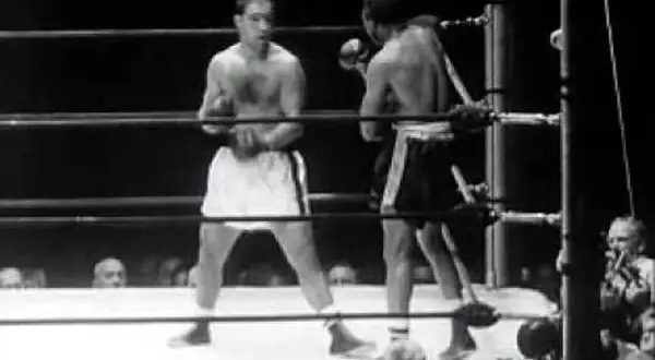 Two boxers in a ring. One boxer, possibly Rocky Marciano, is in the foreground, his reach evident as he prepares to strike.