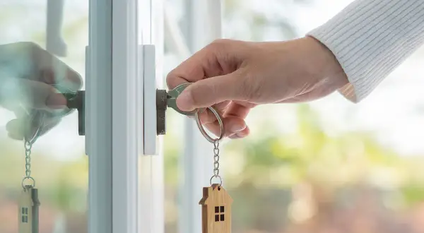 Mano insertando llave con llavero de casa en cerradura. El reflejo muestra la acción de vender casa alquilada.