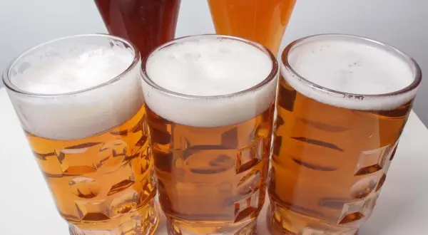 Tre bicchieri di birra dorata con schiuma bianca, uno più scuro e uno arancione sullo sfondo. Un invito a scoprire la differenza tra pils e lager.
