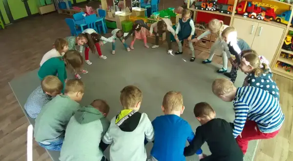 Dzieci w przedszkolu biorą udział w zabawach integracyjnych, tworząc krąg i wykonując ćwiczenia.