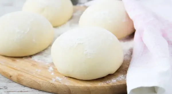 Kulki ciasta na pizzę, posypane mąką, leżą na desce. Zastanawiasz się, czy można mrozić ciasto na pizzę? Tak, można!