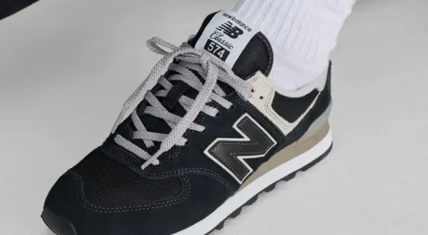 Klasyczne czarne buty sportowe new balance wl 574 z szarymi sznurówkami i beżowymi akcentami, noszone z białymi skarpetkami z logo.