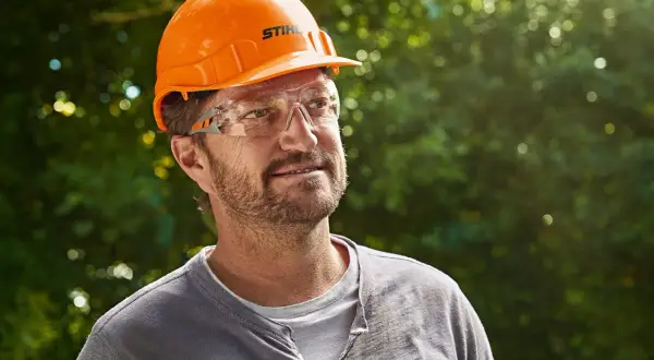 Hombre con casco naranja y gafas de seguridad, listo para usar su epi desbrozadora.