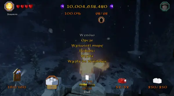 Menu gry Lego Hobbit. Widać postać Saurona, serduszka życia, punkty, procent ukończenia, a także opcje takie jak "Dodatki" i "Wznow", które mogą być powiązane z lego hobbit kody.