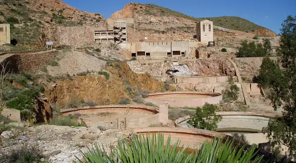Ruinas de las minas Rodalquilar, con edificios abandonados y balsas circulares en un paisaje árido bajo un cielo azul.
