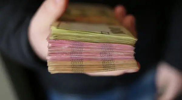 Gruba paczka banknotów, różowych i żółtych, trzymana w dłoni. To zabezpieczenie finansowe, które daje poczucie bezpieczeństwa.