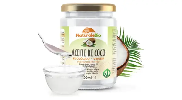 Un frasco de aceite de coco NaturaleBio, con una cuchara vertiendo el aceite en un cuenco. El aceite de coco es bueno para el pelo.