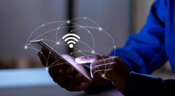Dłoń dotyka ekranu smartfona, nad którym unosi się grafika symbolizująca sieć i sygnał Wi-Fi. To połączenie z apn plus.