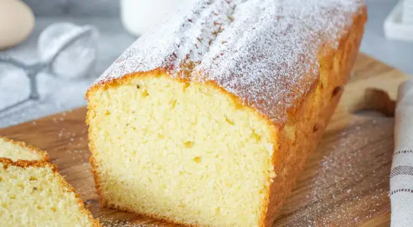 Ein saftiger Rührkuchen, bestäubt mit Puderzucker, ideal für einfache Kuchen Rezepte. Daneben liegen zwei Scheiben.