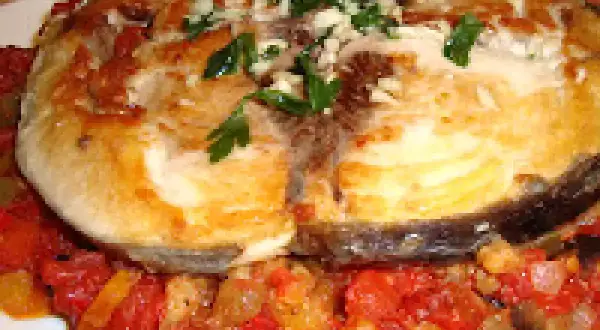 Rodaja de pescado blanco, posiblemente mero, servida sobre un sofrito de verduras y hierbas. Un delicioso plato de sam de atún.