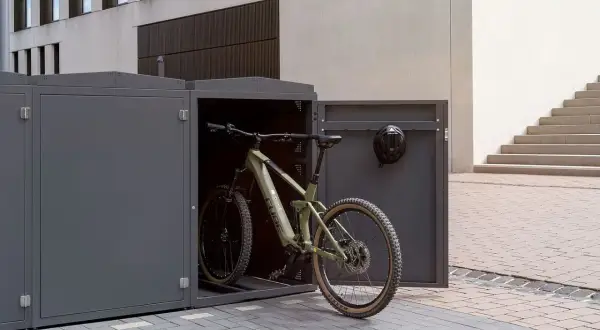 Ein grünes Mountainbike steht in einem modernen, grauen Fahrrad-Stellplatz. Ein Helm hängt an der Tür.