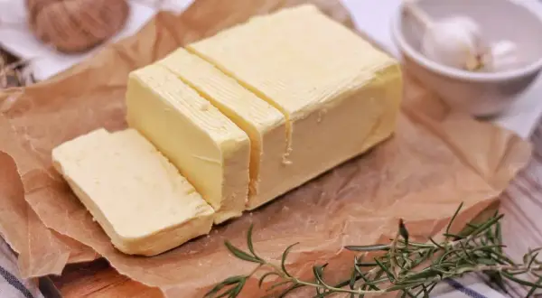 Smörblock skuret i bitar på bakplåtspapper, med rosmarin och vitlök i bakgrunden. Tänk dig att detta smör förvandlas till klarifierat smör, eller ghee, för en rikare smak.