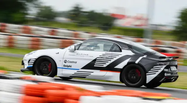 Biało-czarne Alpine A110 z logotypami Castrol i Delphi pędzi po torze wyścigowym, zostawiając za sobą rozmyte bariery.