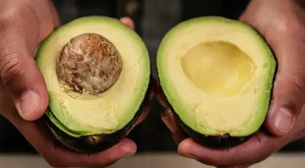 Dłonie trzymają połówki awokado. Jedna z nich ma pestkę, druga jest pusta. Idealne do guacamole, gdy wiesz, jak zmiękczyć awokado.