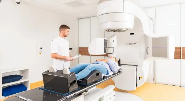Frau liegt auf Behandlungsliege für Prostata-Bestrahlung. Arzt überwacht den Vorgang. Alkohol ist hier fehl am Platz.