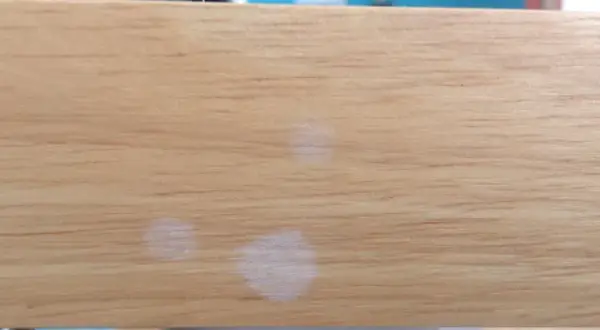 Trois petites taches blanches sur une surface en bois clair, comme des traces laissées par des gouttes d'eau séchées.