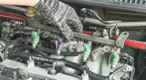 Main d'un mécanicien ganté manipulant le rail d'injection pour tester injecteur diesel.