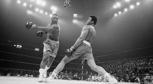 Two boxers clash in a dramatic moment. One out boxer throws a punch while the other dodges, the crowd watching intently.