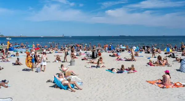 Tłumy ludzi na plaży, opalanie i kąpiel w morzu. Zastanawiasz się, ile kosztuje nocleg nad morzem w sezonie?