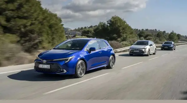 Niebieska Toyota Corolla hatchback, model hybrydowy, jedzie po krętej drodze wśród zielonych wzgórz.
